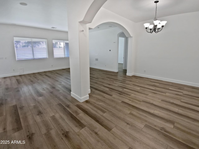 interior space with arched walkways, a notable chandelier, baseboards, and wood finished floors