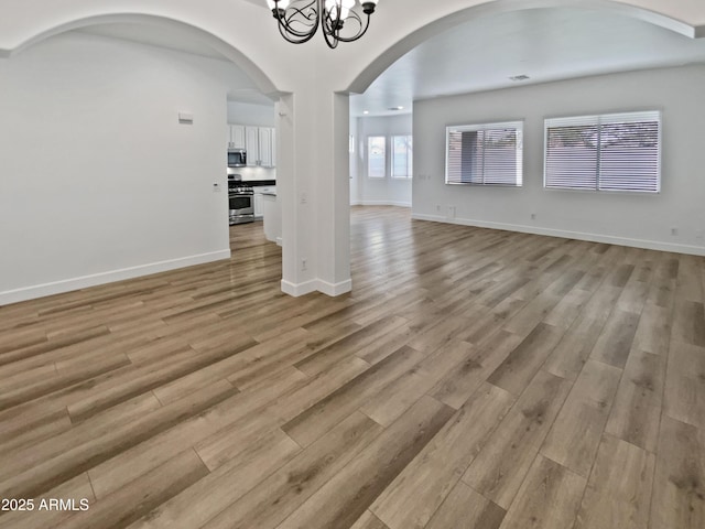 empty room with an inviting chandelier, light wood-style flooring, and baseboards