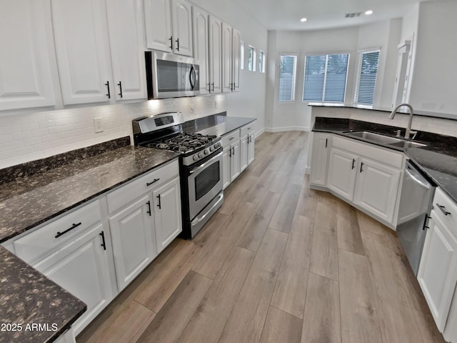 kitchen with light wood-style flooring, a sink, tasteful backsplash, appliances with stainless steel finishes, and white cabinets