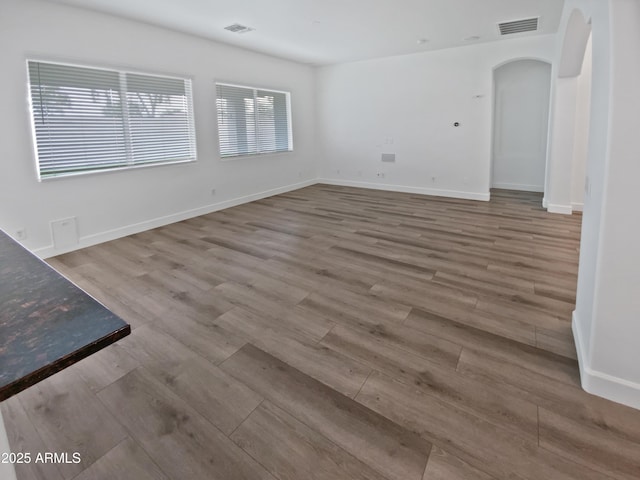 unfurnished room featuring arched walkways, visible vents, and wood finished floors