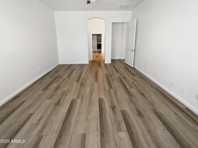 unfurnished bedroom featuring visible vents, arched walkways, baseboards, and wood finished floors