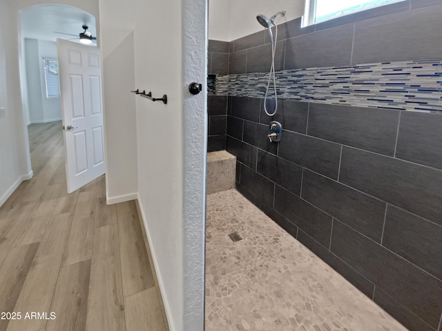 bathroom with ceiling fan, tiled shower, baseboards, and wood finished floors