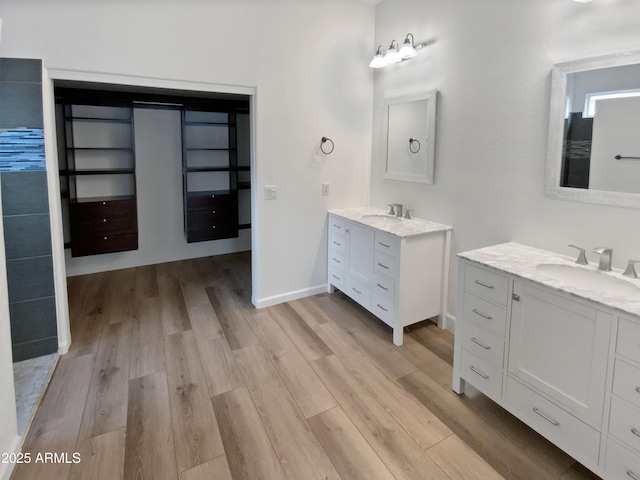 full bath featuring a sink, baseboards, two vanities, and wood finished floors