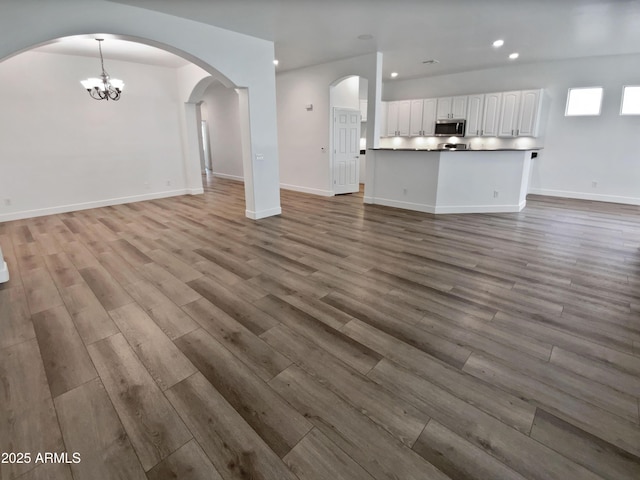 unfurnished living room featuring recessed lighting, baseboards, an inviting chandelier, and wood finished floors