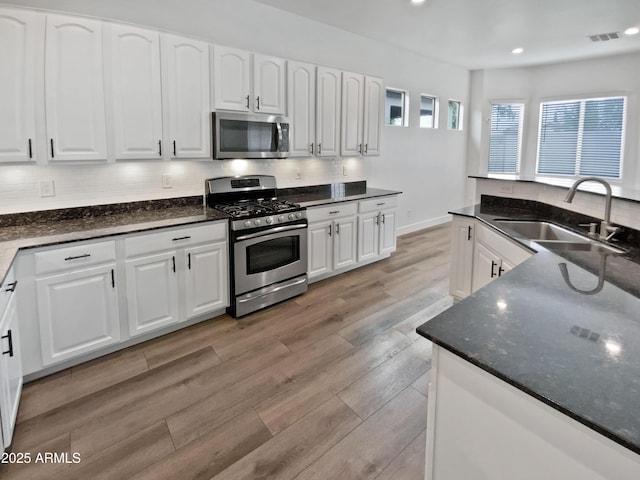 kitchen featuring decorative backsplash, appliances with stainless steel finishes, light wood-type flooring, and a sink