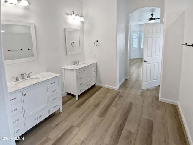 bathroom featuring wood finished floors, two vanities, baseboards, and a sink