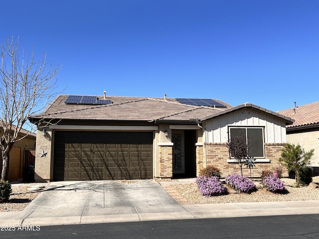 view of front of property featuring brick siding, solar panels, an attached garage, board and batten siding, and driveway