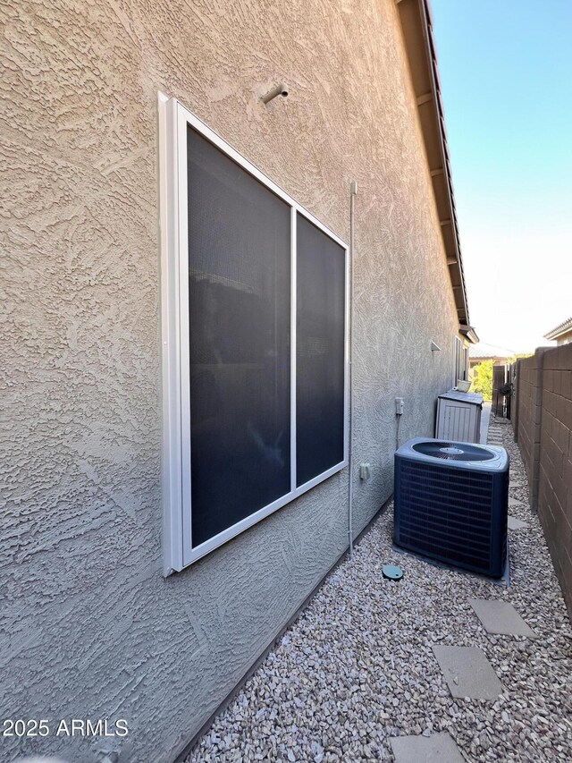 view of property exterior featuring central AC unit, fence, and stucco siding