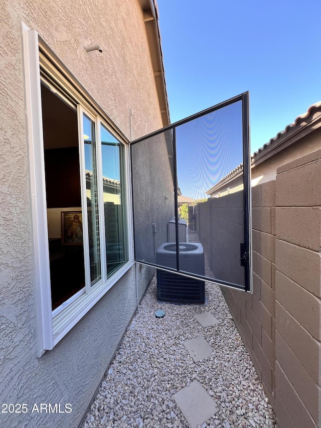 view of side of property featuring central AC, fence, and stucco siding