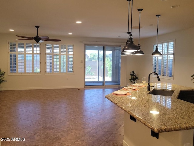 kitchen featuring baseboards, light stone counters, hanging light fixtures, a sink, and recessed lighting