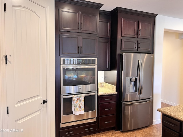 kitchen with baseboards, appliances with stainless steel finishes, light stone counters, and dark brown cabinets