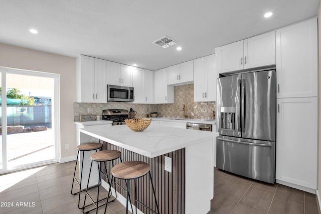 kitchen with stainless steel appliances, white cabinetry, a kitchen bar, sink, and a center island