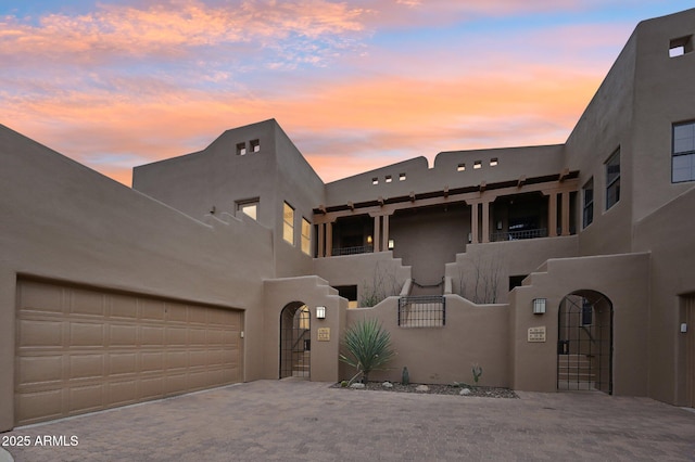 adobe home featuring decorative driveway, an attached garage, fence, and a gate