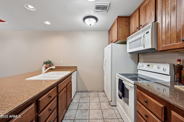 kitchen with brown cabinetry, white appliances, visible vents, and a sink