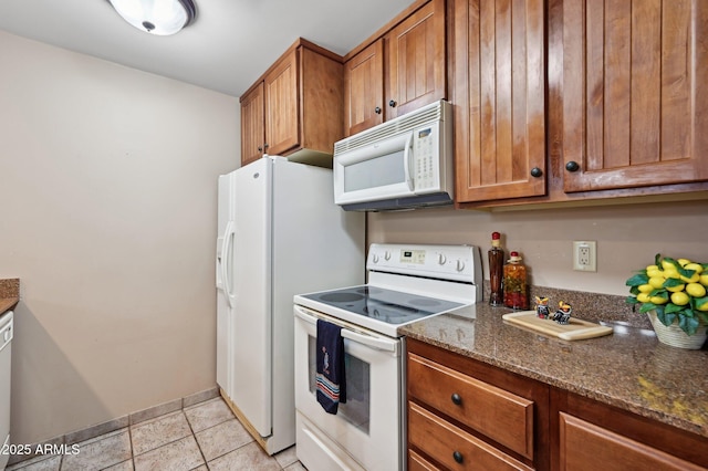 kitchen featuring white appliances, light tile patterned floors, dark stone counters, and brown cabinetry