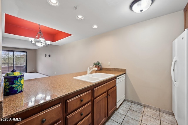 kitchen featuring brown cabinets, a raised ceiling, an inviting chandelier, a sink, and white appliances