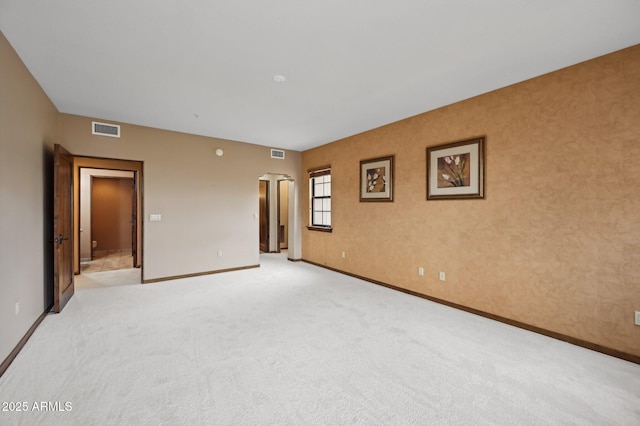 empty room featuring arched walkways, light colored carpet, visible vents, and baseboards