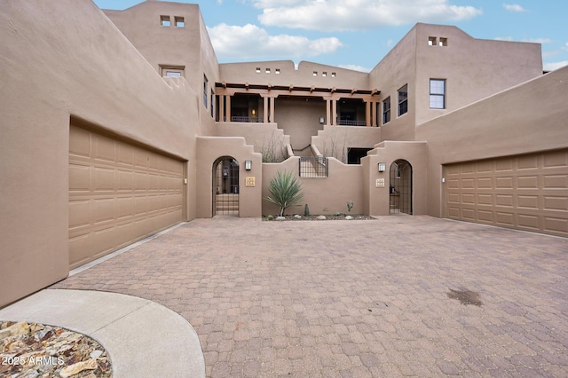 adobe home with a garage, a gate, and stucco siding