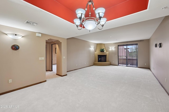 unfurnished living room featuring visible vents, a fireplace with raised hearth, baseboards, an inviting chandelier, and carpet