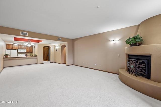 unfurnished living room featuring a notable chandelier, light colored carpet, visible vents, a fireplace with raised hearth, and baseboards