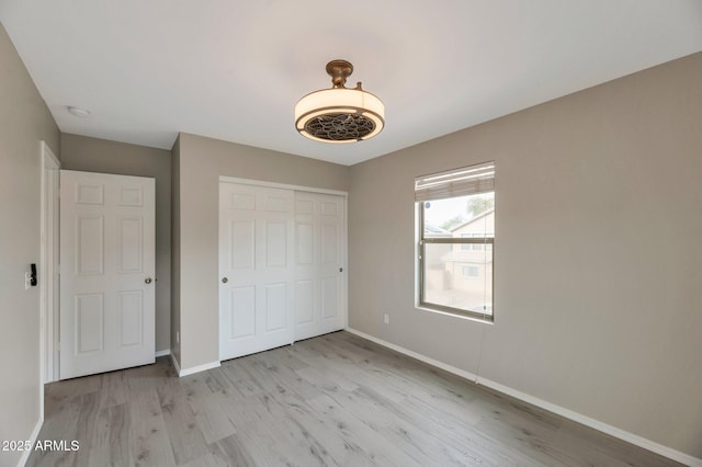 unfurnished bedroom featuring light wood finished floors, a closet, and baseboards