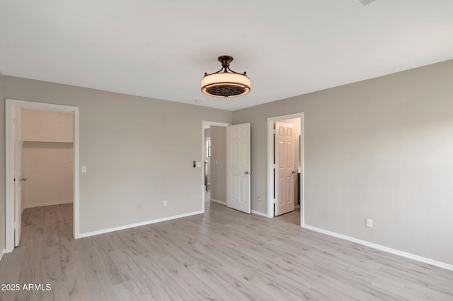 unfurnished bedroom with baseboards, light wood-style floors, and a spacious closet