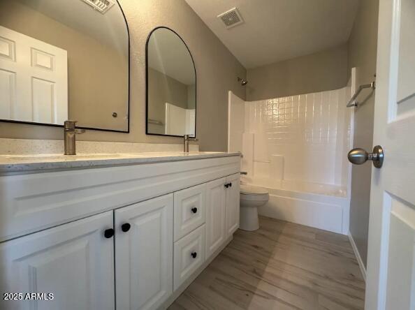 bathroom with washtub / shower combination, visible vents, double vanity, a sink, and toilet