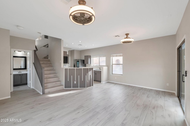 unfurnished living room with stairway, baseboards, light wood finished floors, recessed lighting, and a sink