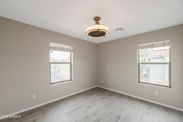 empty room featuring visible vents, baseboards, and light wood finished floors