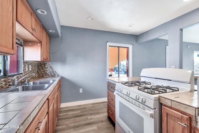 kitchen featuring dark wood-type flooring, sink, backsplash, white gas range oven, and tile countertops