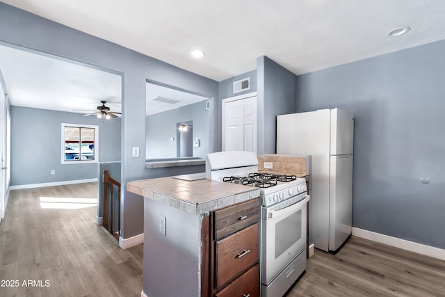 kitchen with ceiling fan, tile counters, white appliances, light wood-type flooring, and a kitchen island