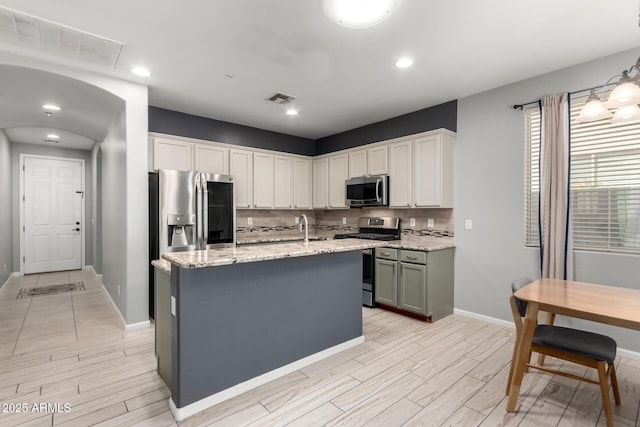 kitchen with light stone countertops, appliances with stainless steel finishes, white cabinetry, an island with sink, and decorative backsplash