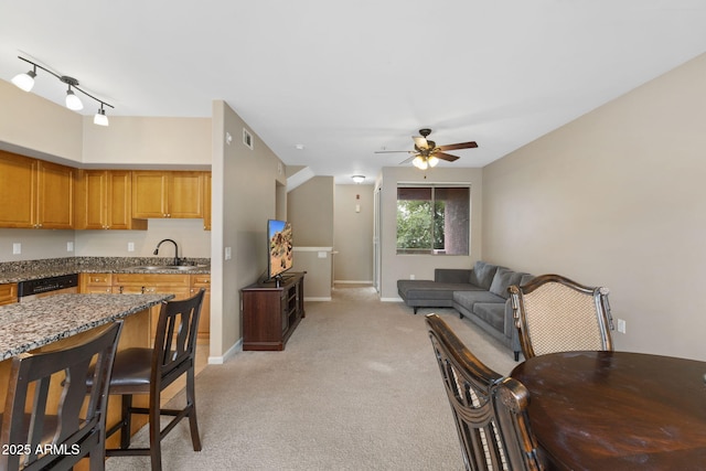 kitchen featuring sink, light colored carpet, ceiling fan, dark stone countertops, and stainless steel dishwasher