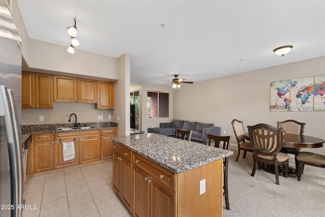 kitchen with sink, light tile patterned floors, stainless steel fridge, dark stone countertops, and a kitchen island