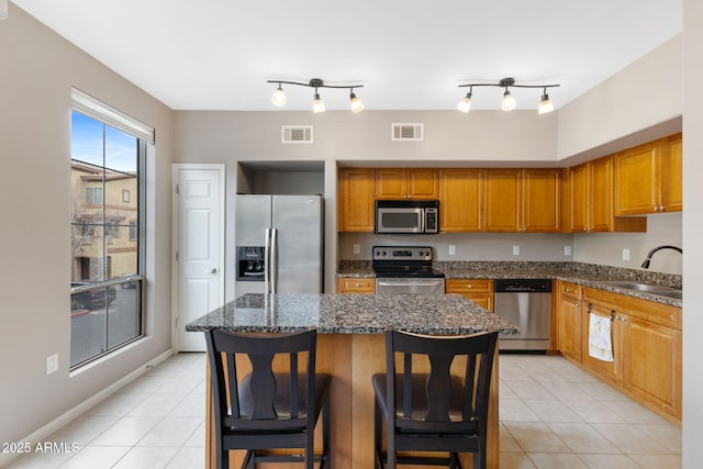 kitchen with light tile patterned flooring, appliances with stainless steel finishes, sink, a breakfast bar area, and a center island