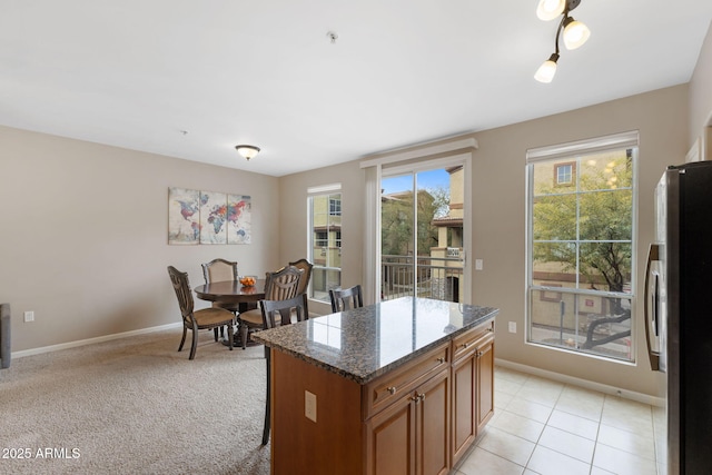 kitchen with dark stone countertops, stainless steel fridge, a center island, and light carpet