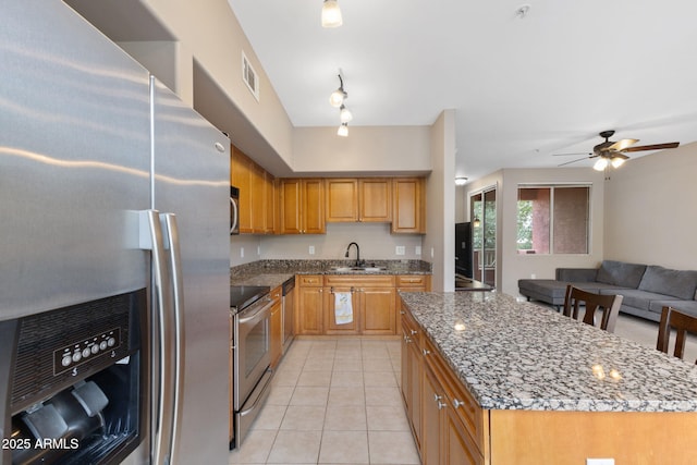 kitchen with light tile patterned floors, sink, stone counters, stainless steel appliances, and a kitchen island