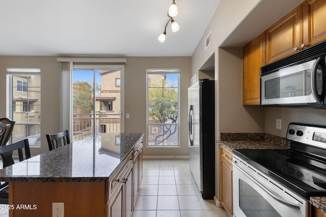 kitchen featuring light tile patterned flooring, a kitchen island, a breakfast bar, dark stone countertops, and stainless steel appliances