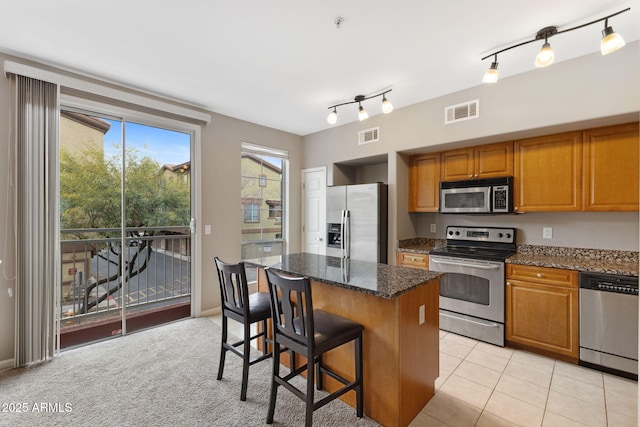 kitchen featuring light tile patterned flooring, a kitchen bar, dark stone countertops, a kitchen island, and stainless steel appliances