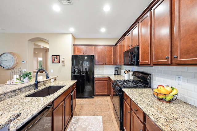 kitchen with arched walkways, a sink, light stone countertops, black appliances, and backsplash