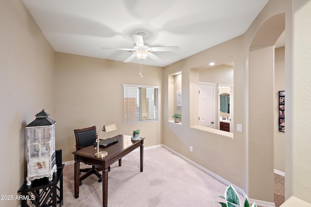 office area featuring ceiling fan, arched walkways, light colored carpet, a sink, and baseboards