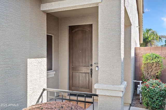 doorway to property featuring fence and stucco siding