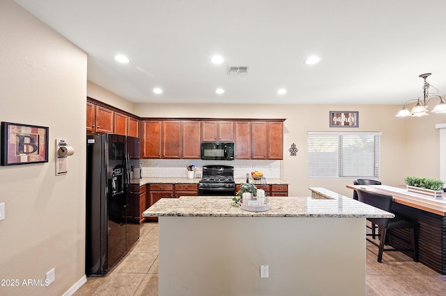 kitchen featuring pendant lighting, backsplash, a kitchen island, light stone countertops, and black appliances