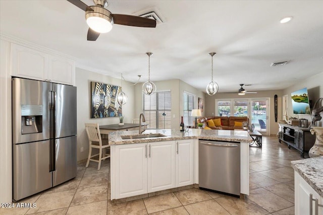 kitchen with light stone countertops, white cabinetry, sink, hanging light fixtures, and appliances with stainless steel finishes