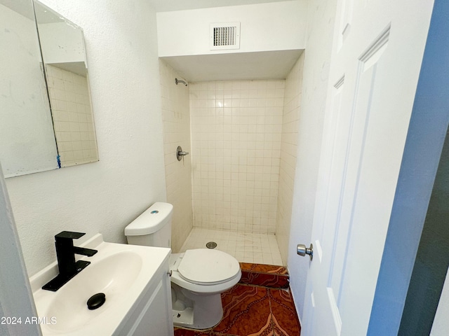 bathroom featuring a tile shower, vanity, and toilet