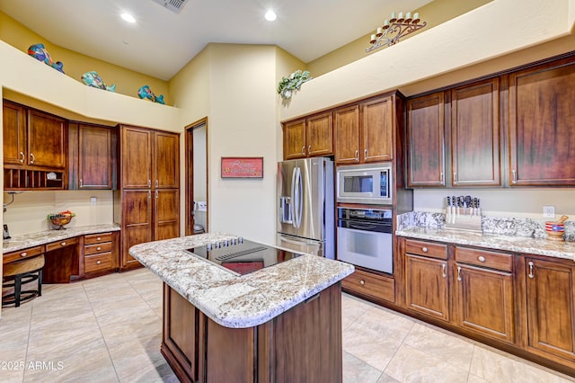 kitchen with built in study area, appliances with stainless steel finishes, light stone counters, a center island, and recessed lighting