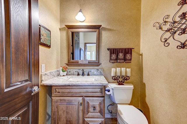 bathroom featuring toilet, vanity, and a textured wall