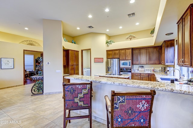 kitchen with a peninsula, visible vents, appliances with stainless steel finishes, and light stone counters