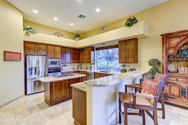 kitchen featuring visible vents, appliances with stainless steel finishes, light stone counters, a peninsula, and a sink