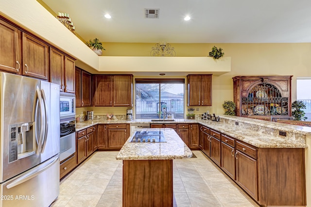 kitchen featuring white appliances, visible vents, a kitchen island, light stone counters, and a peninsula